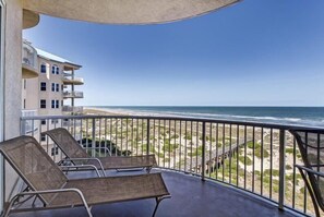 A balcony with two lounge chairs overlooking a beach and ocean.