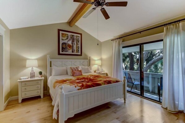 A bedroom with a bed, bedside tables, a ceiling fan, a window with curtains, and a balcony with a chair.