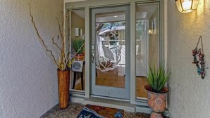 A modern entrance with a glass door, decorative plants, and a wall-mounted light fixture.