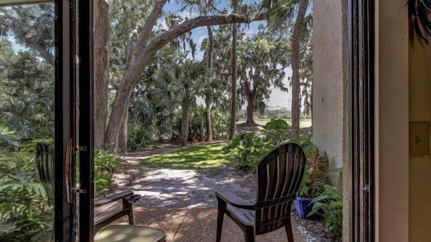 A patio with a wooden table and chairs, surrounded by lush greenery and trees.