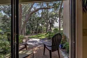 A patio with a wooden table and chairs, surrounded by lush greenery and trees.