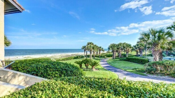 A landscaped garden with a pathway leading to the beach, palm trees, and a view of the ocean. - 1418-windsong (Fernandina Beach)