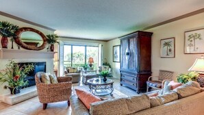 A spacious living room with a fireplace, comfortable seating, and decorative plants. - 1418-windsong (Fernandina Beach)