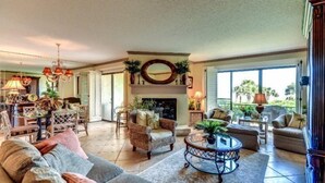 A spacious living room with a fireplace, comfortable seating, and large windows offering a view of the outdoors. - 1418-windsong (Fernandina Beach)