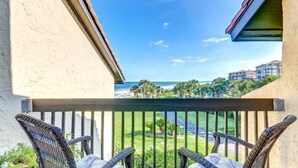 A balcony with wicker chairs and a view of the ocean and palm trees. - 1418-windsong (Fernandina Beach)