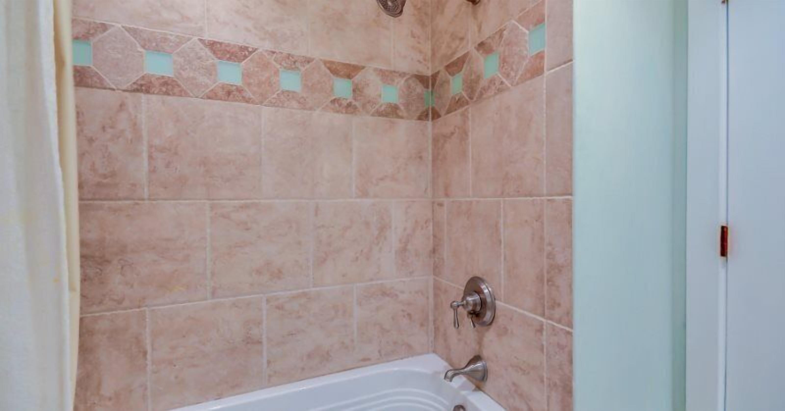 A bathroom with beige tiles, a bathtub, and a shower area.