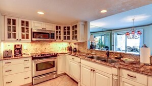 A kitchen with white cabinets, a double oven, a microwave, and a large window with a view of the outdoors. - 1418-windsong (Fernandina Beach)
