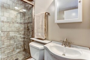 A bathroom with a glass shower enclosure, a toilet, a sink, and a mirror. - 1179-beach-walker (Fernandina Beach)