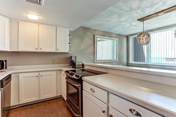 A modern kitchen with white cabinetry, a built-in oven, and a window with blinds.