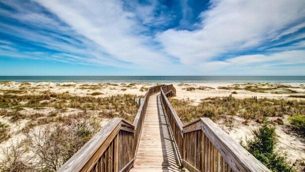 A wooden boardwalk leading to a beach with dunes and a clear sky. - 234-sandcastles (Fernandina Beach)