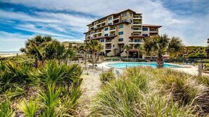 A multi-story hotel with a pool surrounded by tropical vegetation. - 234-sandcastles (Fernandina Beach)
