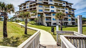 A multi-story hotel with balconies, a grassy lawn, and a wooden walkway leading to the entrance. - 234-sandcastles (Fernandina Beach)