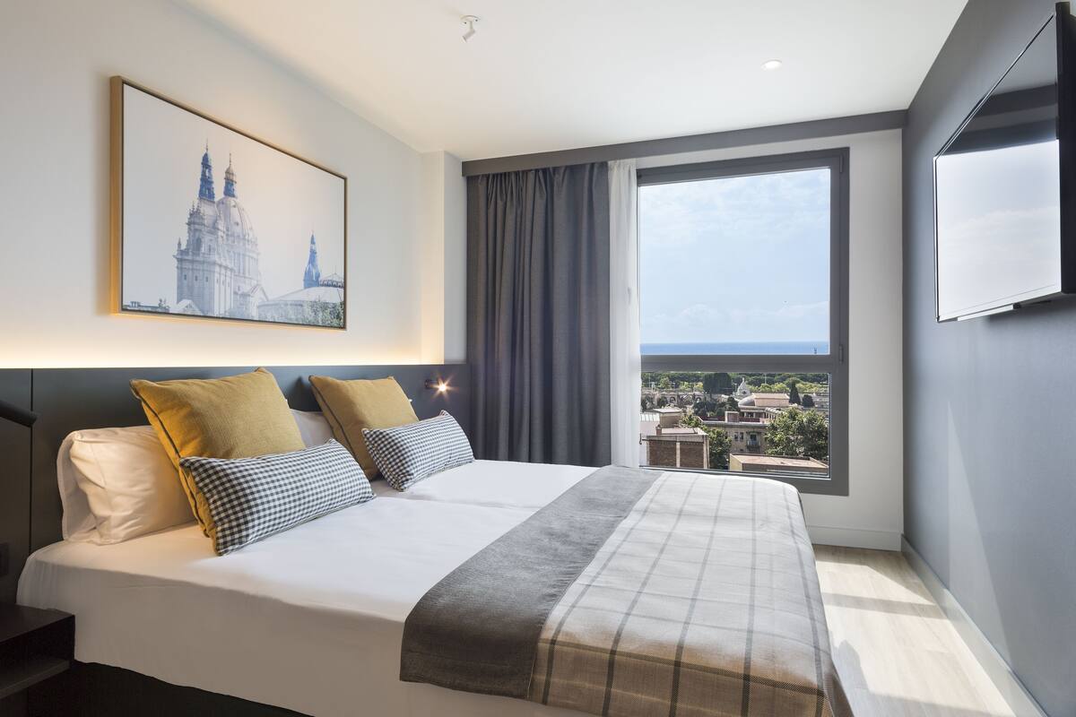 Une chambre d’hôtel moderne avec un grand lit, une vue sur la ville, un tableau encadré au mur et un téléviseur à écran plat.