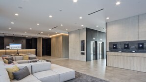 A modern lobby with a sectional sofa, a reception desk, and a large screen. - Hotel Acta Voraport (Barcelona)