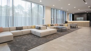 Amplia sala de estar con un sofá modular grande, una mesa de centro y una mesa de comedor. Hay ventanas grandes con cortinas, una cocina con mostrador y un techo moderno con iluminación empotrada.