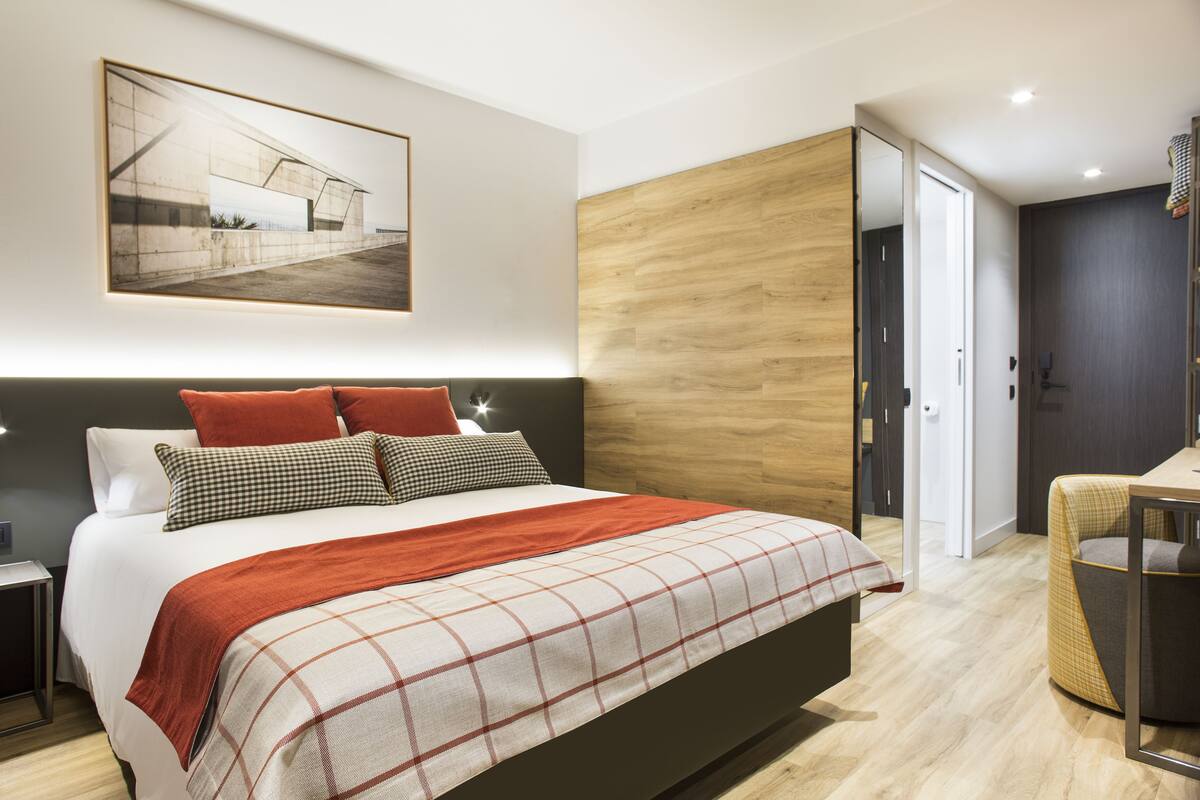 Une chambre à coucher moderne avec un grand lit, un mur d’accent en bois et un tableau encadré au-dessus du lit.