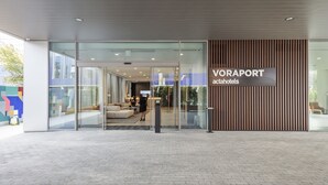 Una entrada de hotel moderna con fachada de vidrio, un letrero que dice "VORAPORT actahotels" y una zona de estar en el interior.