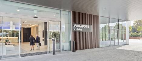 A modern hotel entrance with a glass facade, a wooden panel design, and a sign reading "VORAPORT actahotels".