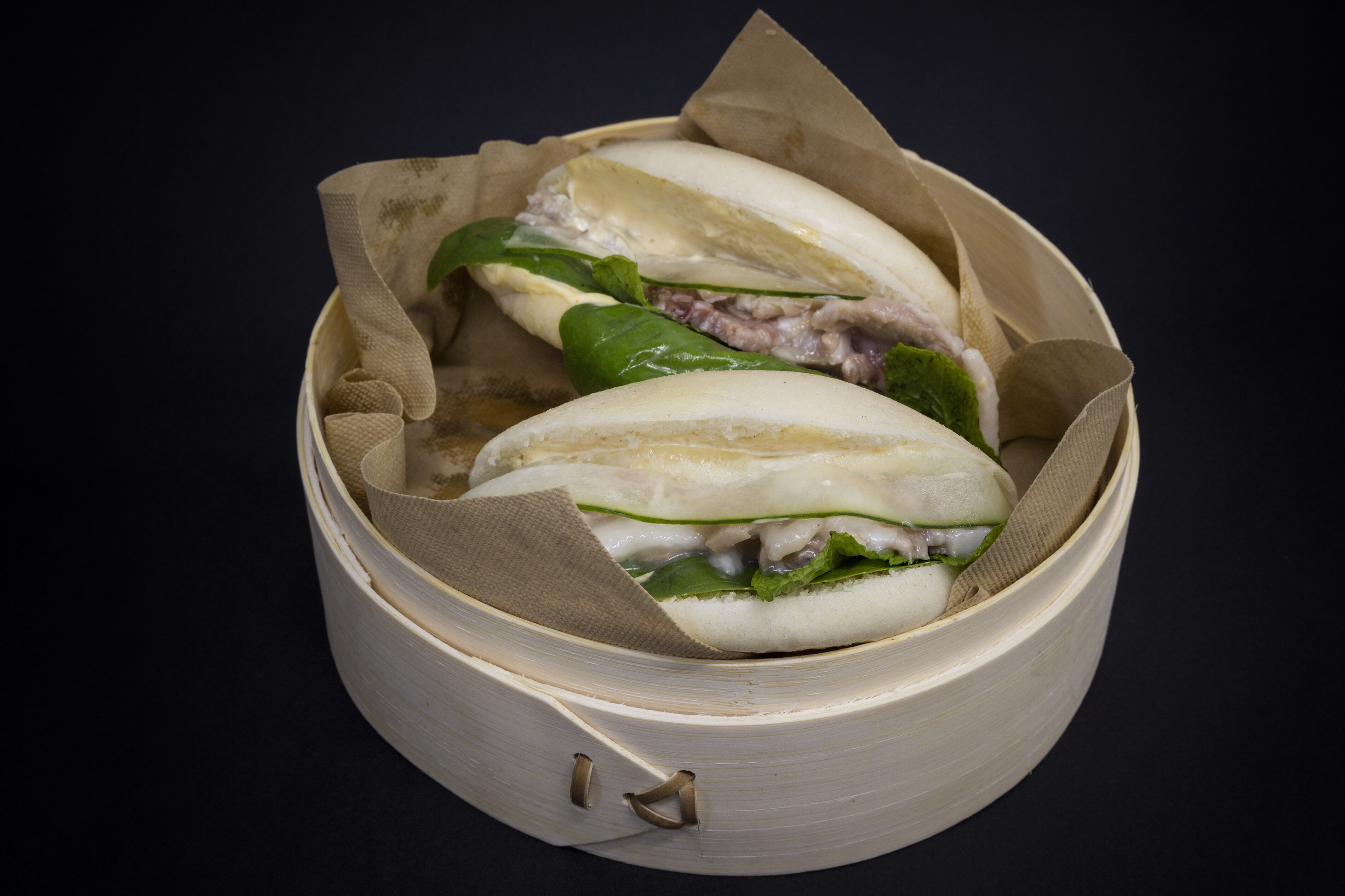 A bamboo steamer containing two steamed buns with fillings.