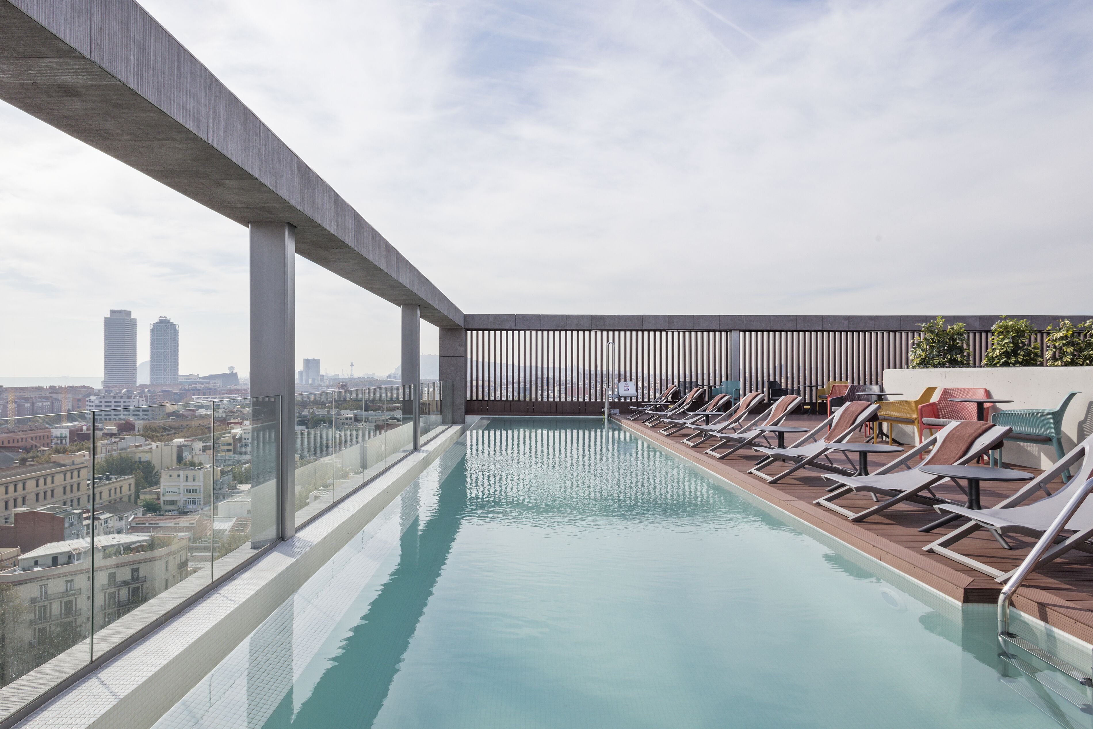 A rooftop infinity pool with lounge chairs and a city view.