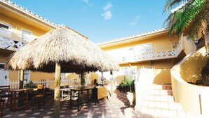 A courtyard with a thatched-roof structure, outdoor seating, and a staircase leading to a balcony. - The Palms (Hollywood)