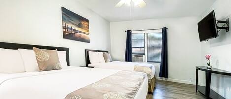 A hotel room with two beds, a ceiling fan, a painting, a TV, and a window with curtains.