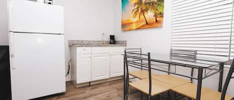 A kitchen with white cabinets, a white refrigerator, a wooden table, and a chair.