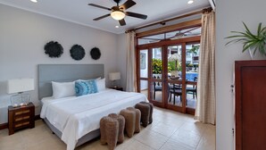 A hotel room with a bed, a ceiling fan, a nightstand, and a view of an outdoor pool area. - Ground Floor Unit in Beautiful Beachfront Complex (Jacó)