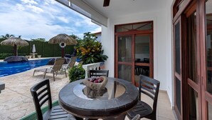 A covered outdoor area with a pool, chairs, a table with fruit, and a ceiling fan. - Ground Floor Unit in Beautiful Beachfront Complex (Jacó)