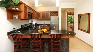A kitchen with a central island, wooden cabinets, a refrigerator, and a dining area with chairs. - Charming Garden View Apt in Exclusive Community (Jacó)