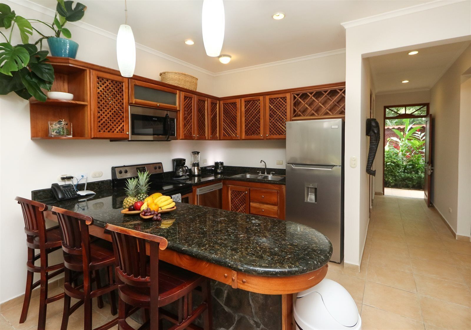 A kitchen with a granite countertop, wooden cabinets, a stainless steel refrigerator, and a dining area with chairs.