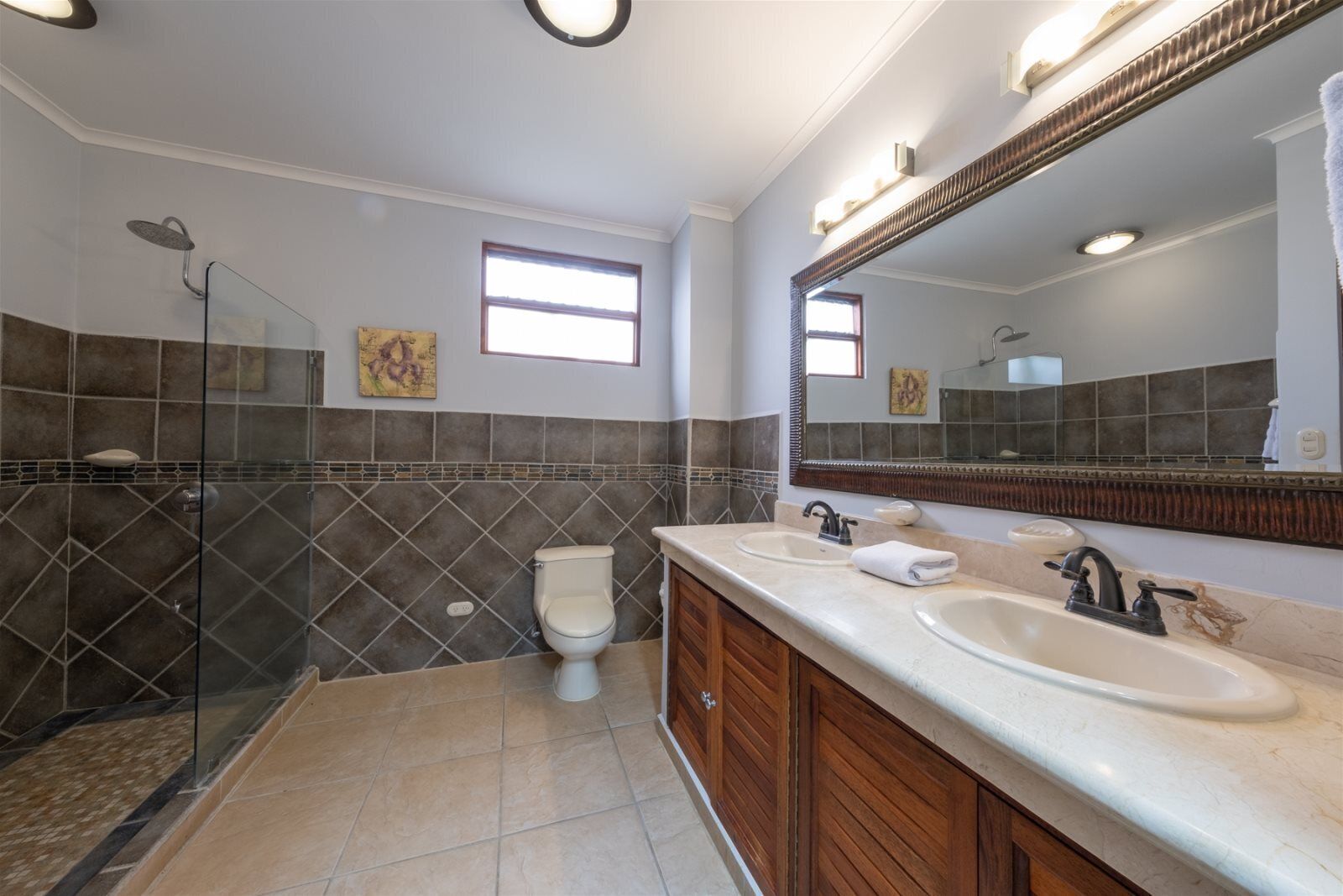 Een badkamer met een douche, twee wastafels, een toilet en een grote spiegel.