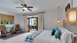 A bedroom with a bed, two wicker chairs, a ceiling fan, a window with curtains, and a view of an outdoor dining area. - Magnificent and Spacious Poolside 3BR Condo (Jacó)