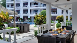 A dining area with a table set for two, overlooking a pool and a white building with balconies. - Magnificent and Spacious Poolside 3BR Condo (Jacó)