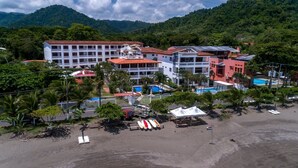A hotel with multiple buildings, a beach, and mountains in the background. - Magnificent and Spacious Poolside 3BR Condo (Jacó)
