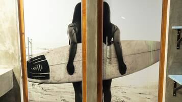 Uma pessoa segurando uma prancha de surf em um quarto com piso de concreto e vigas de madeira.