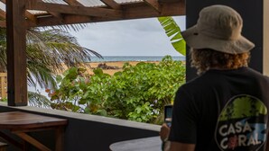 Una persona sentada a una mesa de madera con vista a una playa y palmeras.