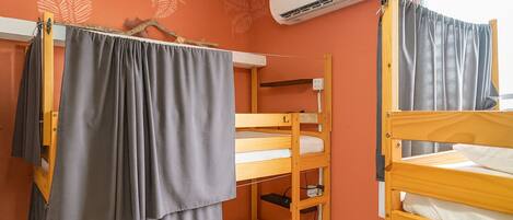 A dormitory room with bunk beds, an air conditioning unit, and a window with curtains.