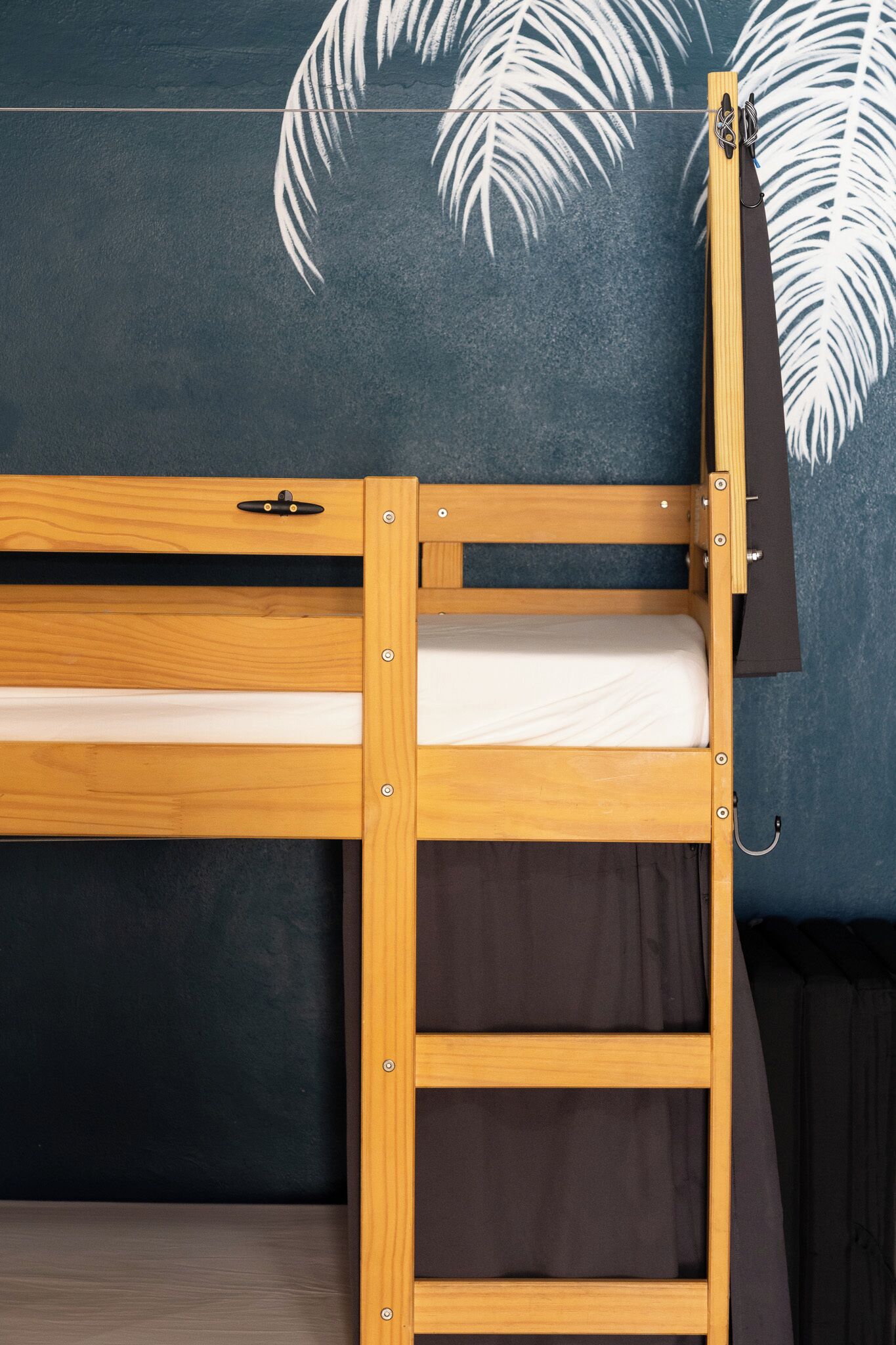 A bunk bed with a wooden frame and a ladder, against a wall with a leaf pattern.