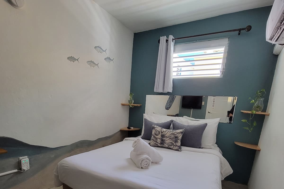 Un dormitorio con cama, mesita de noche, espejo, ventana con cortinas y aire acondicionado de pared.