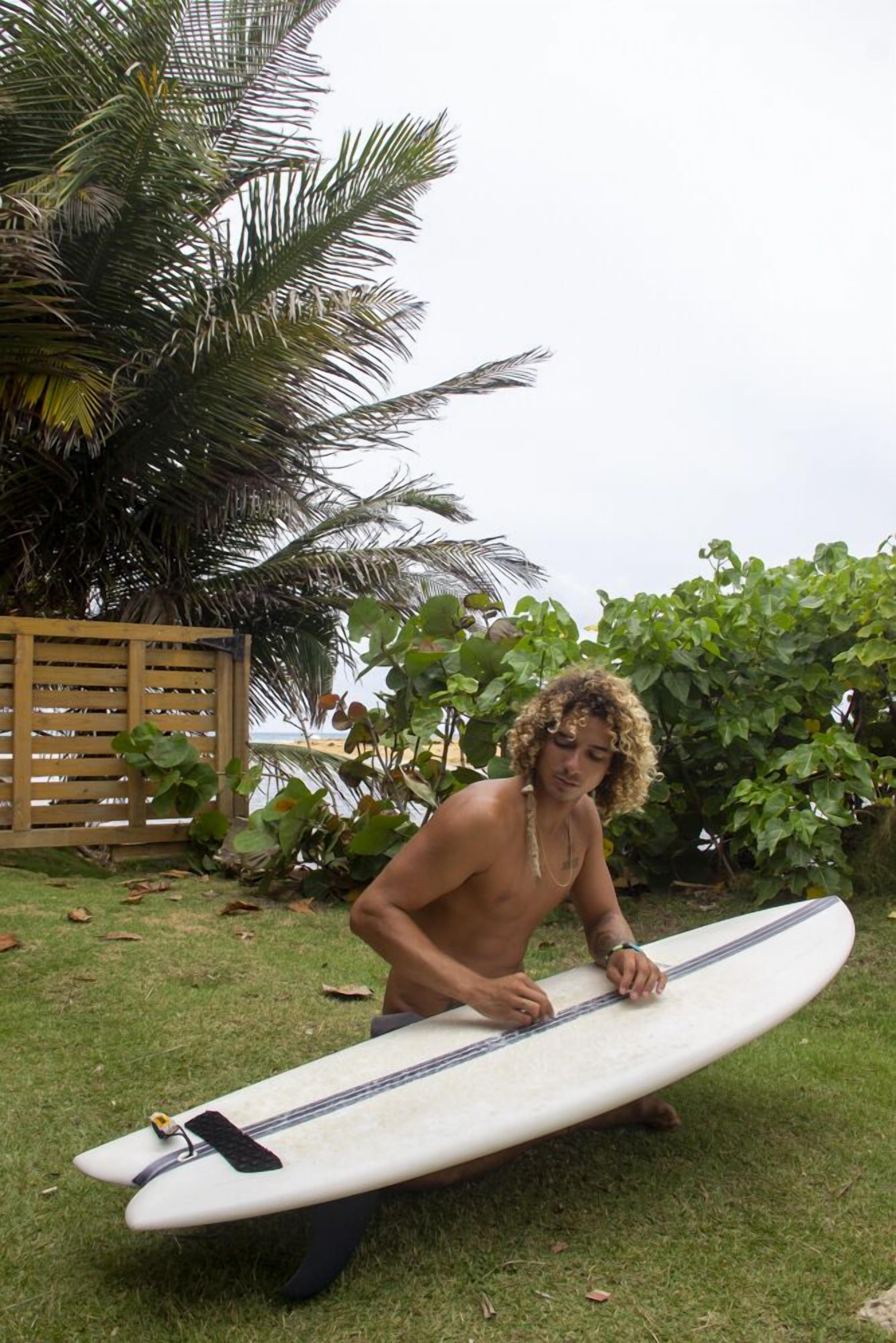 Una persona arrodillada sobre césped sosteniendo una tabla de surf.
