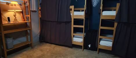 A room with bunk beds, a desk with a lamp, and a window with blinds.