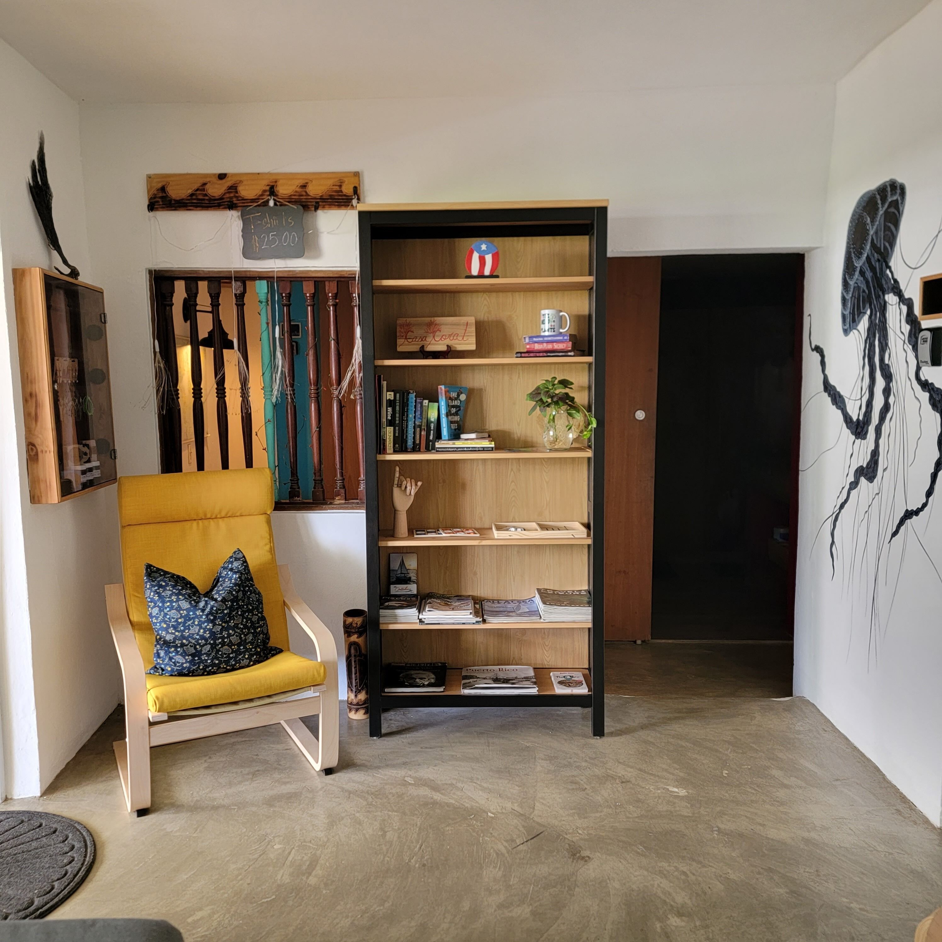 Una habitación con un sillón amarillo, una estantería de madera y una pared con un cuadro abstracto de gran tamaño.