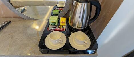 Un carrito de desayuno con dos tazas, una cafetera y diversos alimentos en una habitación de hotel.