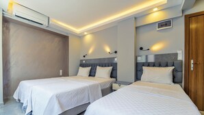 Habitació d'hotel amb dos llits individuals, una porta de fusta i un aparell d'aire condicionat.