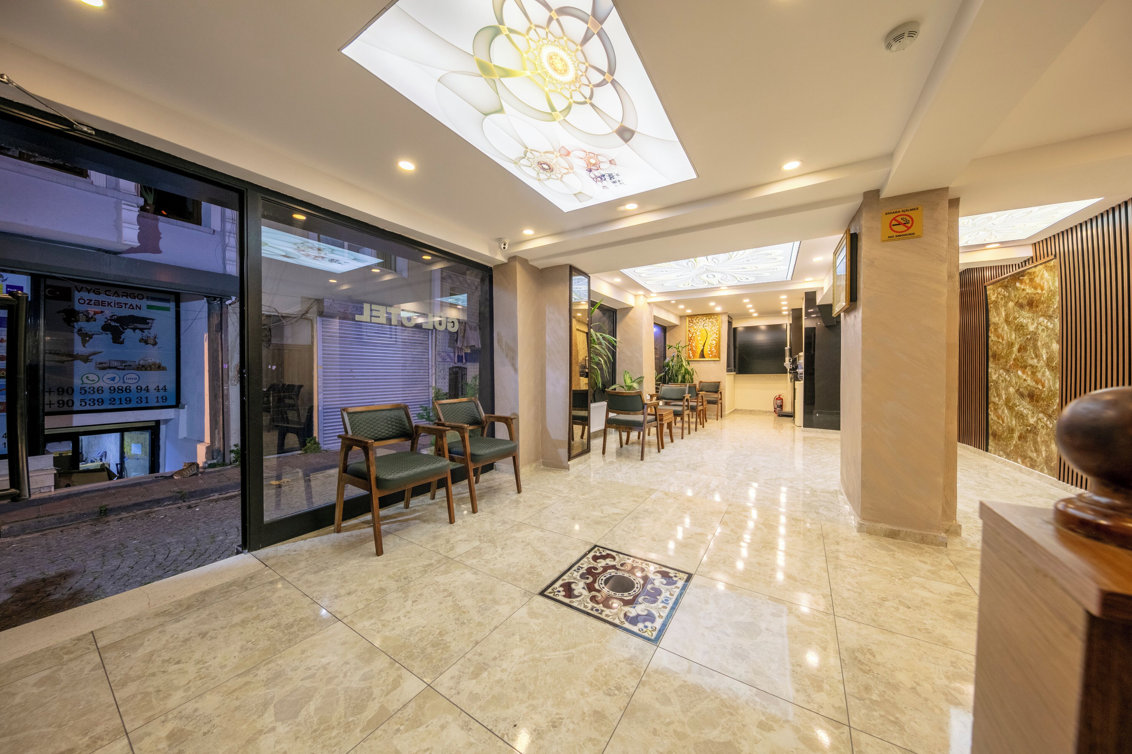A hotel lobby with a reception desk, seating area, and a large glass door leading outside.