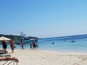 A beach with a yacht docked, people walking along the shore, and a clear blue sky. - Bellamar (Roatan)