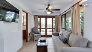 Un vaste espace de vie doté d’un ventilateur de plafond, d’un téléviseur à écran plat, d’un canapé, d’un fauteuil et d’une petite table agrémentée d’une plante.