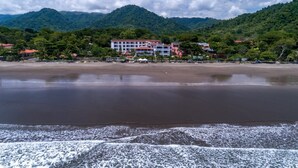 Un hôtel en bord de mer composé de plusieurs bâtiments, doté d’une plage de sable et situé au pied de montagnes.