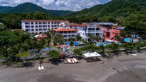 A hotel with multiple buildings, a beach, and mountains in the background. - Lpb-2d (Jacó)